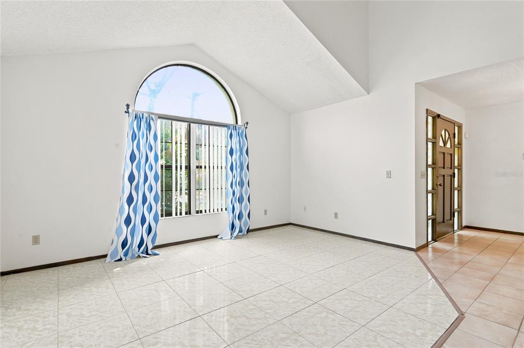 An empty room features white walls, vaulted ceilings, tiled floors, and a large arched window — 1469 MONA DRIVE, KISSIMMEE, FL