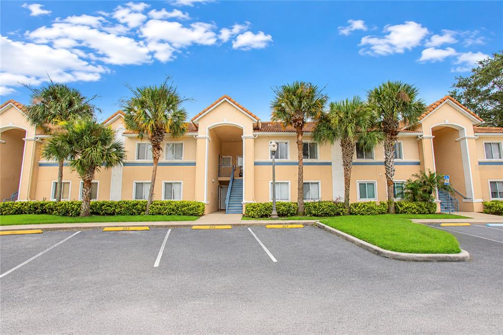 An exterior view of a two-story apartment building with tan stucco walls and blue stairs — 508 VILLA DEL SOL CIRCLE UNIT 204, ORLANDO, FL