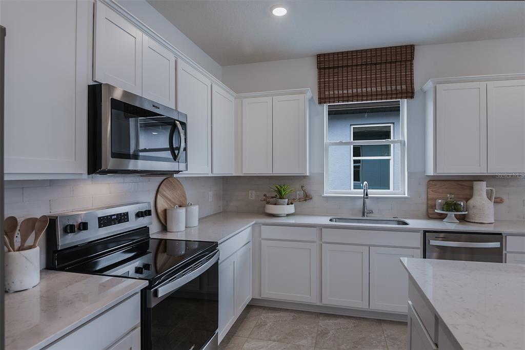 A kitchen features white cabinets, stainless steel appliances, quartz countertops, and a window with blinds — 11124 SYCAMORE GLEN LOOP, THONOTOSASSA, FL