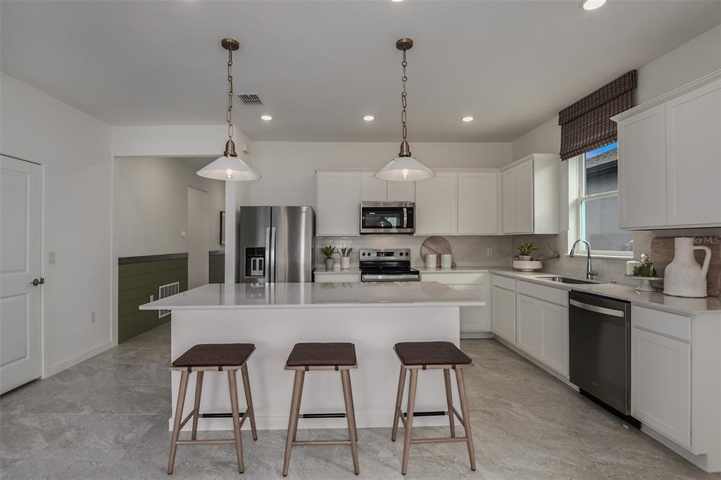A kitchen with white cabinets, a quartz island, three stools, and stainless steel appliances — 11124 SYCAMORE GLEN LOOP, THONOTOSASSA, FL
