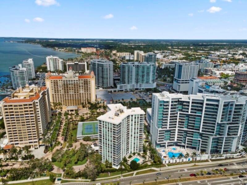 An aerial view of multiple high-rise apartment buildings and a tennis court near a bay — 1111 N GULFSTREAM AVENUE UNIT 6B, SARASOTA, FL