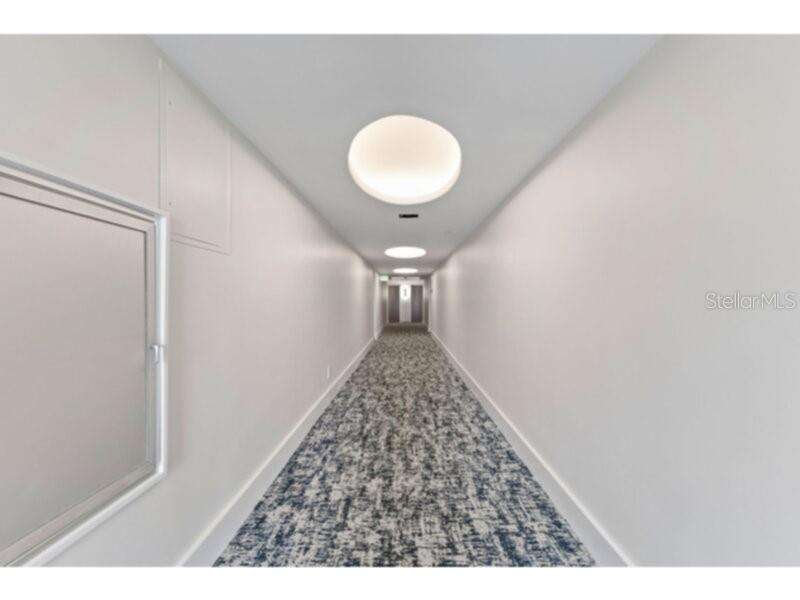 A long, narrow indoor hallway features white walls, recessed circular ceiling lights, and patterned carpet — 1111 N GULFSTREAM AVENUE UNIT 6B, SARASOTA, FL