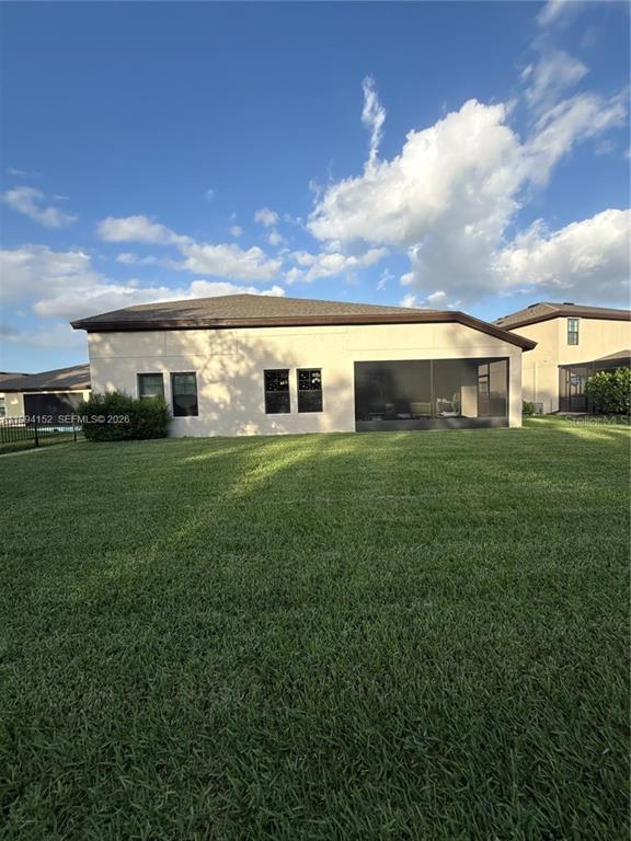 The exterior rear view of a beige house features a screened-in patio and lawn — 9173 WARM SPRINGS CIRCLE, PARRISH, FL