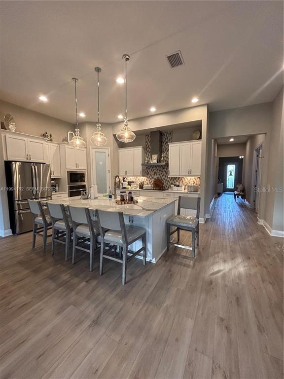 A kitchen features white cabinetry, a large island with bar seating, and light wood flooring — 9173 WARM SPRINGS CIRCLE, PARRISH, FL