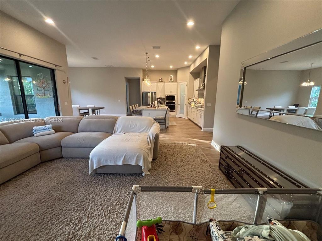 A spacious open-concept living room features a large sectional sofa, carpeted flooring, and a kitchen — 9173 WARM SPRINGS CIRCLE, PARRISH, FL