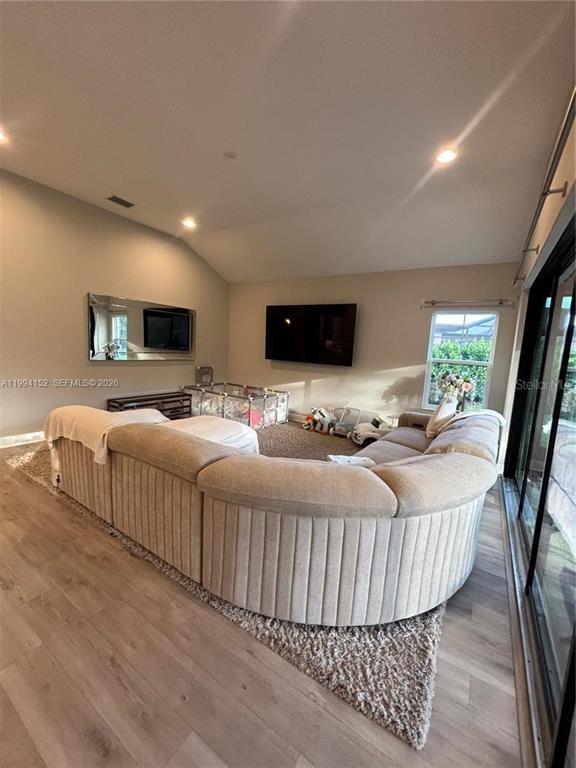 A living room features a large curved sectional sofa, light wood flooring, and a vaulted ceiling — 9173 WARM SPRINGS CIRCLE, PARRISH, FL