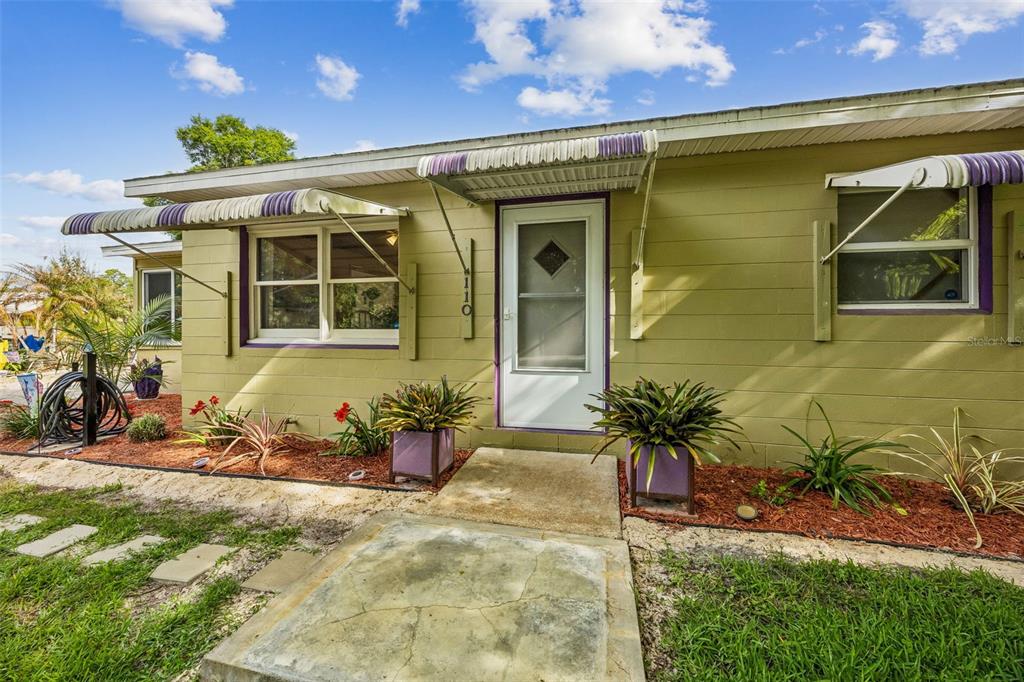 The exterior of a light green house features a white front door and striped awnings — 110 SHAFFER AVENUE, CRESCENT CITY, FL
