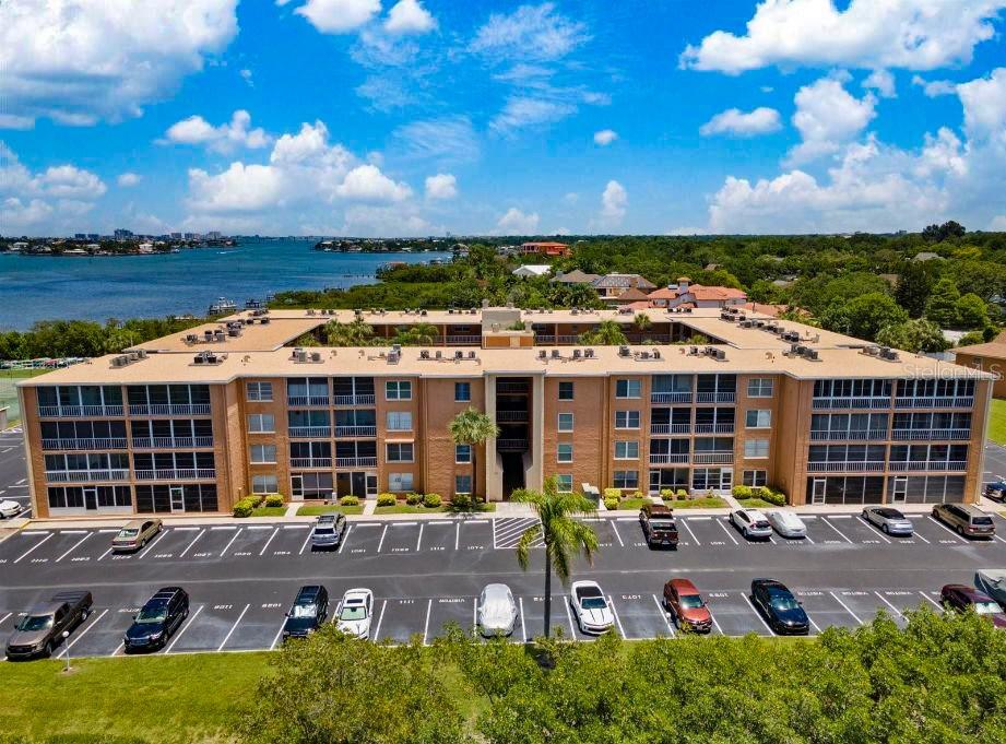 An aerial view shows a multi-story apartment building with a parking lot and waterfront scenery — 12760 INDIAN ROCKS ROAD UNIT 1030 (Furnished), LARGO, FL