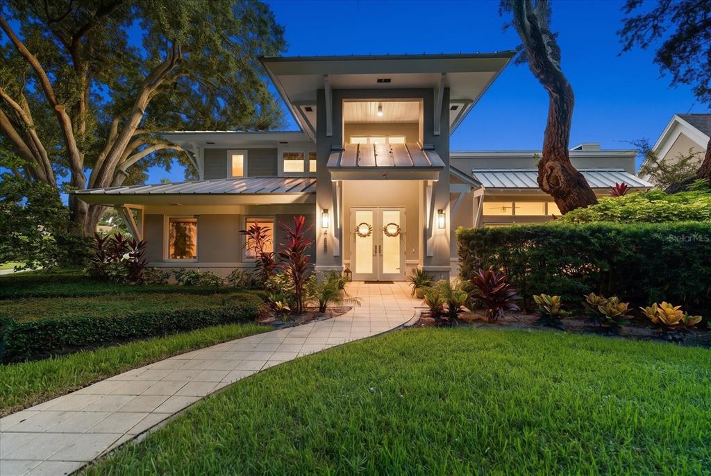 A modern house exterior with a metal roof, large trees, and vibrant landscaping in front — 485 PARK AVENUE, BELLEAIR, FL