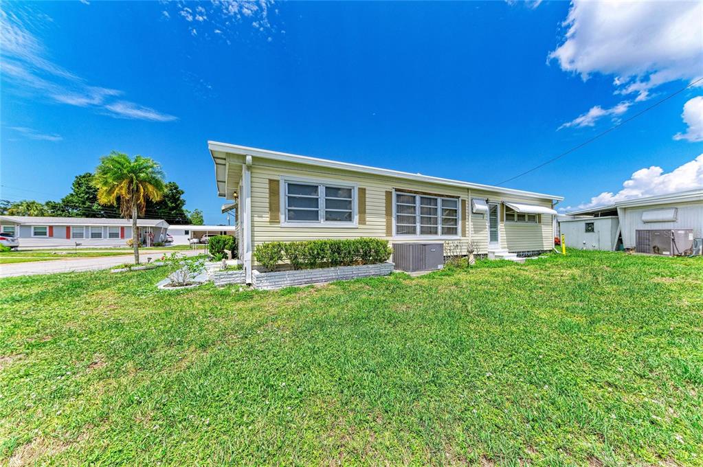 A single-story mobile home with light yellow siding sits on a grassy lot — 1781 OLYMPIA FIELDS STREET, SARASOTA, FL