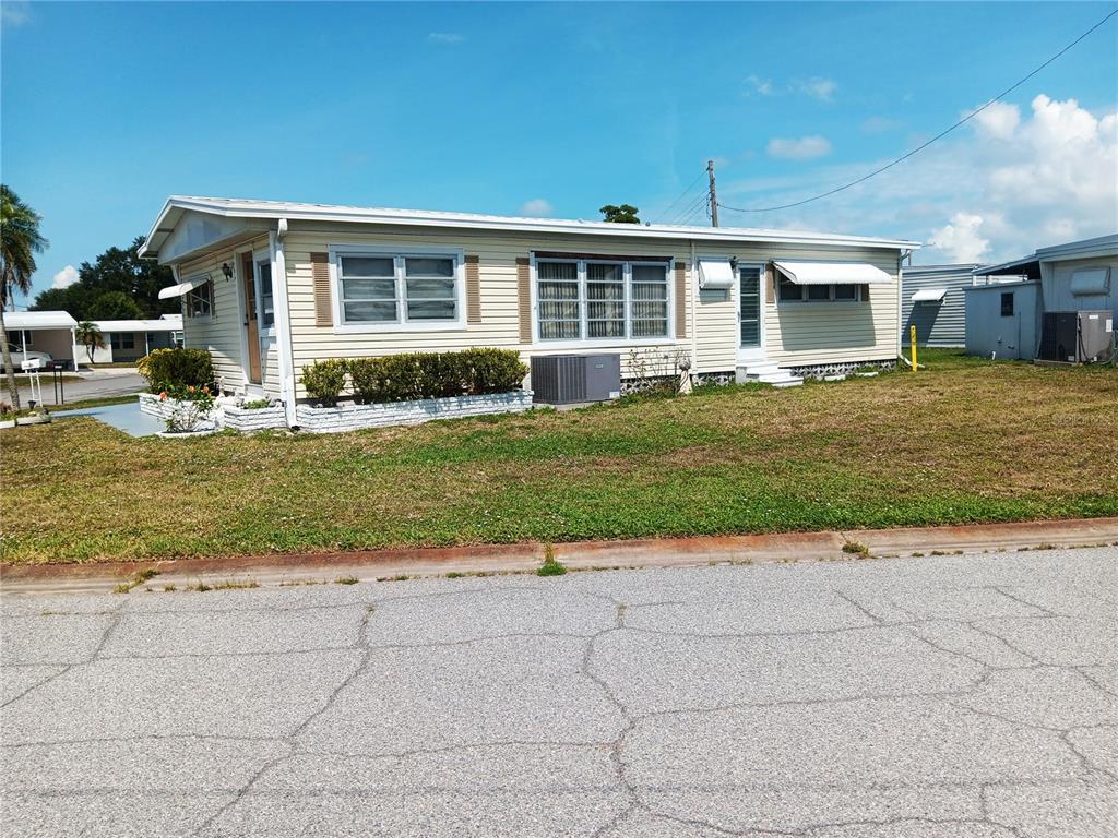 A single-story mobile home with light yellow siding, a carport, and a palm tree — 1781 OLYMPIA FIELDS STREET, SARASOTA, FL