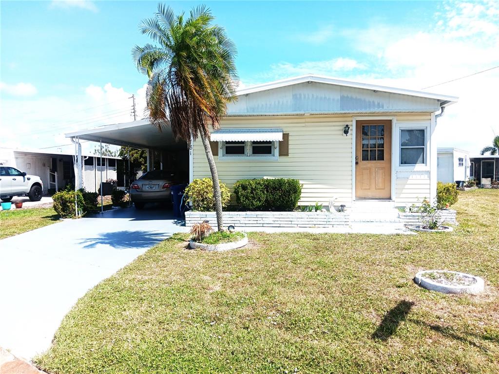 A light yellow mobile home with white trim sits on a grassy lot under a blue sky — 1781 OLYMPIA FIELDS STREET, SARASOTA, FL