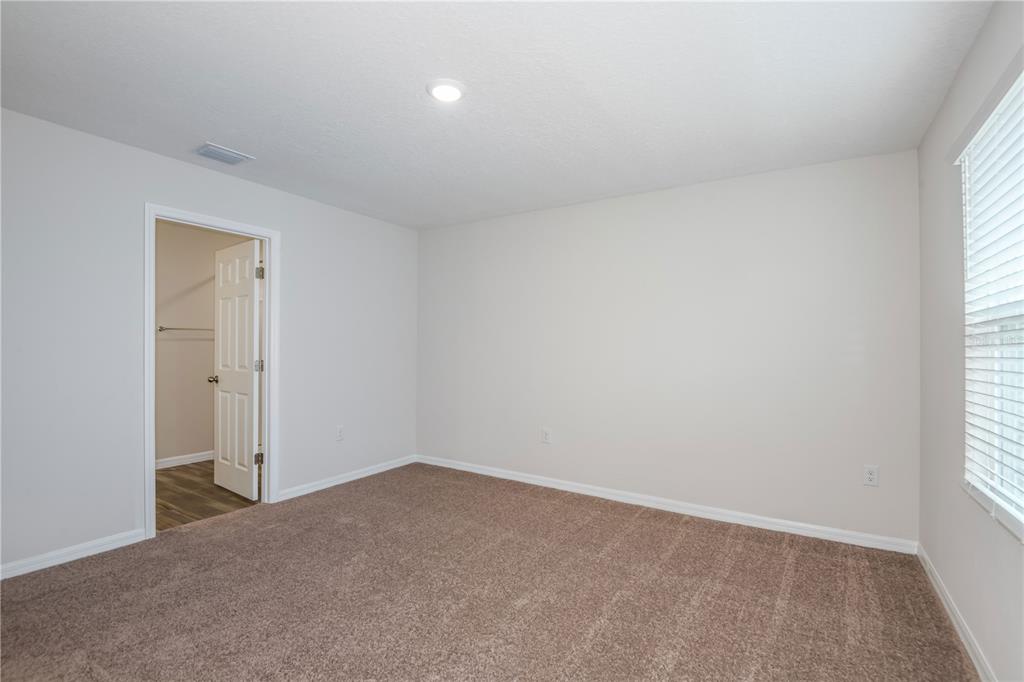 An empty bedroom features beige walls, brown carpeting, a window with blinds, and a closet — 9888 PELICAN COAST DRIVE, DADE CITY, FL