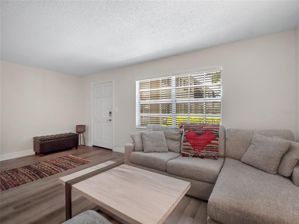 A living room features a sectional sofa, a coffee table, a bench, and a window — 4335 AEGEAN DRIVE UNIT 116A, TAMPA, FL