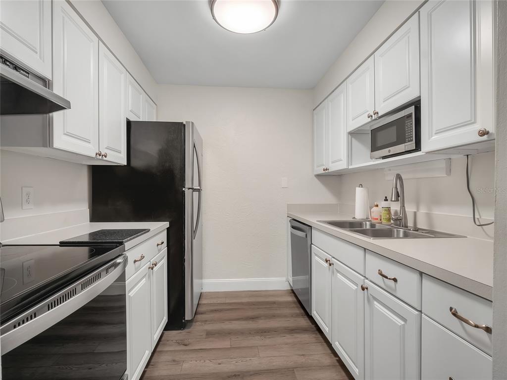 A galley kitchen features white cabinets, stainless steel appliances, and wood-look flooring — 4335 AEGEAN DRIVE UNIT 116A, TAMPA, FL