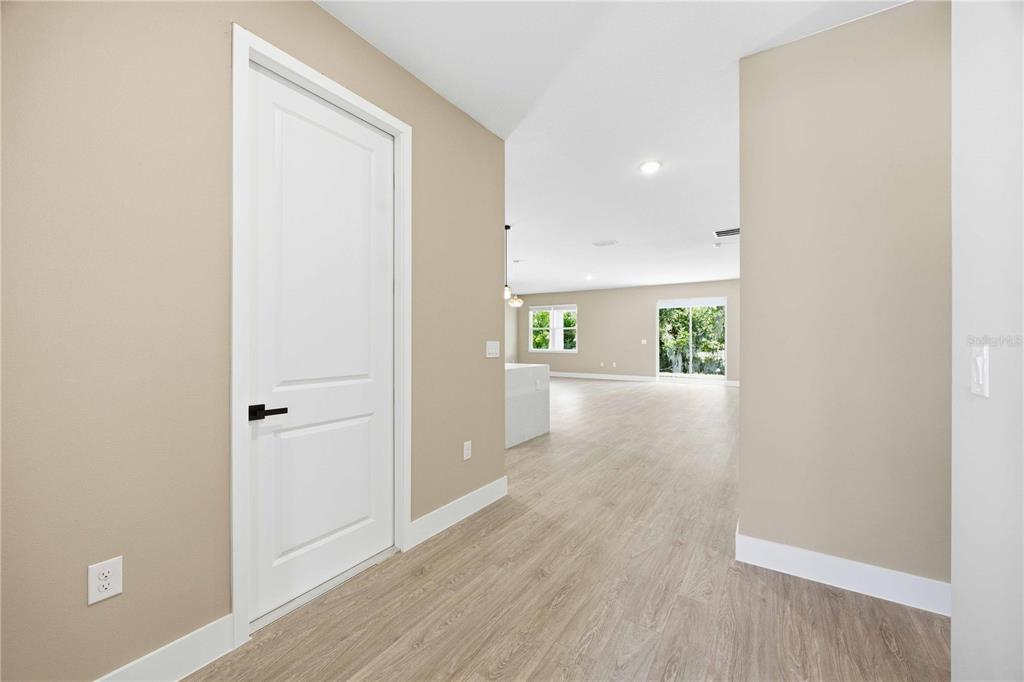A hallway with light wood flooring leads into an open-concept living area with white trim — 2108 RIVER HAWK LOOP, WINTER HAVEN, FL
