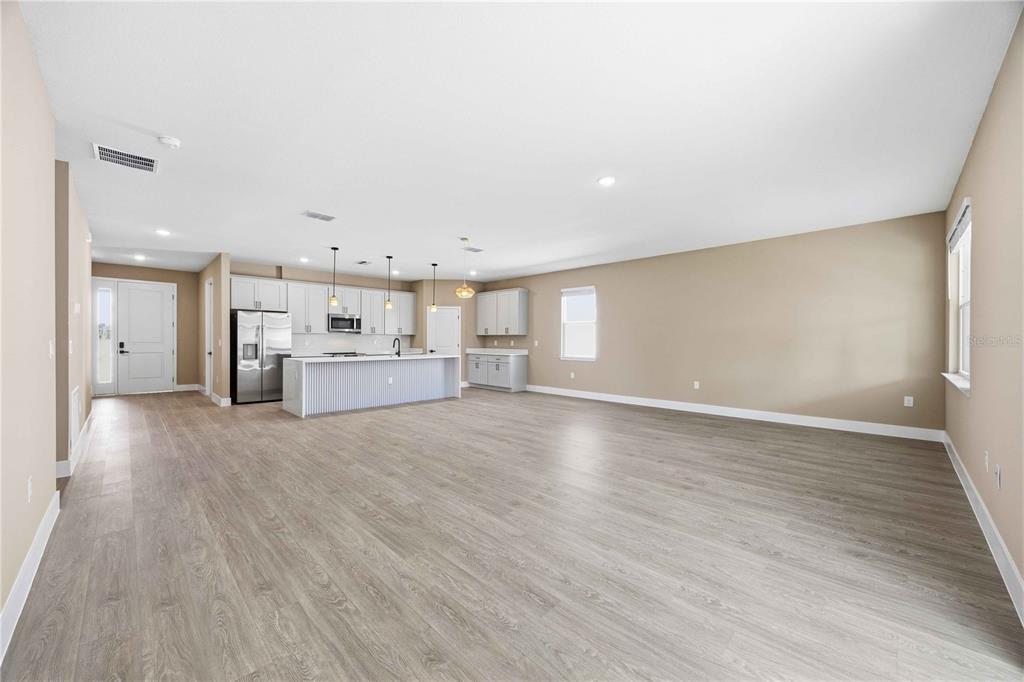 An open-concept living area features light wood-look flooring, a kitchen island, and white cabinetry — 2108 RIVER HAWK LOOP, WINTER HAVEN, FL