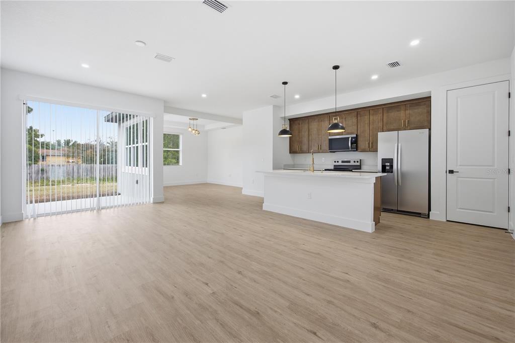 An open-concept kitchen and living area featuring wood-look flooring, white walls, and stainless appliances — 1 OAK TRAIL, OCALA, FL