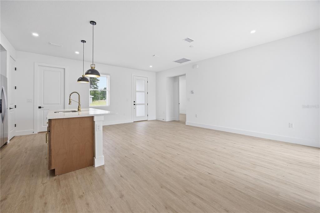 An open-concept kitchen and living area features light wood-look flooring, white walls, and a kitchen island — 1 OAK TRAIL, OCALA, FL