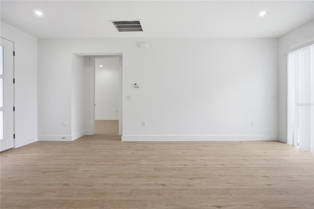A bright, empty room features light wood-look flooring, white walls, and a doorway leading inside — 1 OAK TRAIL, OCALA, FL