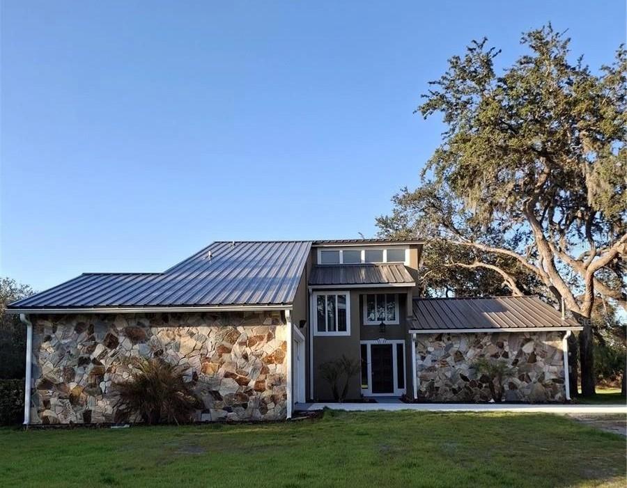 A two-story house with a metal roof, stone facade, and an attached garage — 2598 ENTERPRISE OSTEEN ROAD, OSTEEN, FL