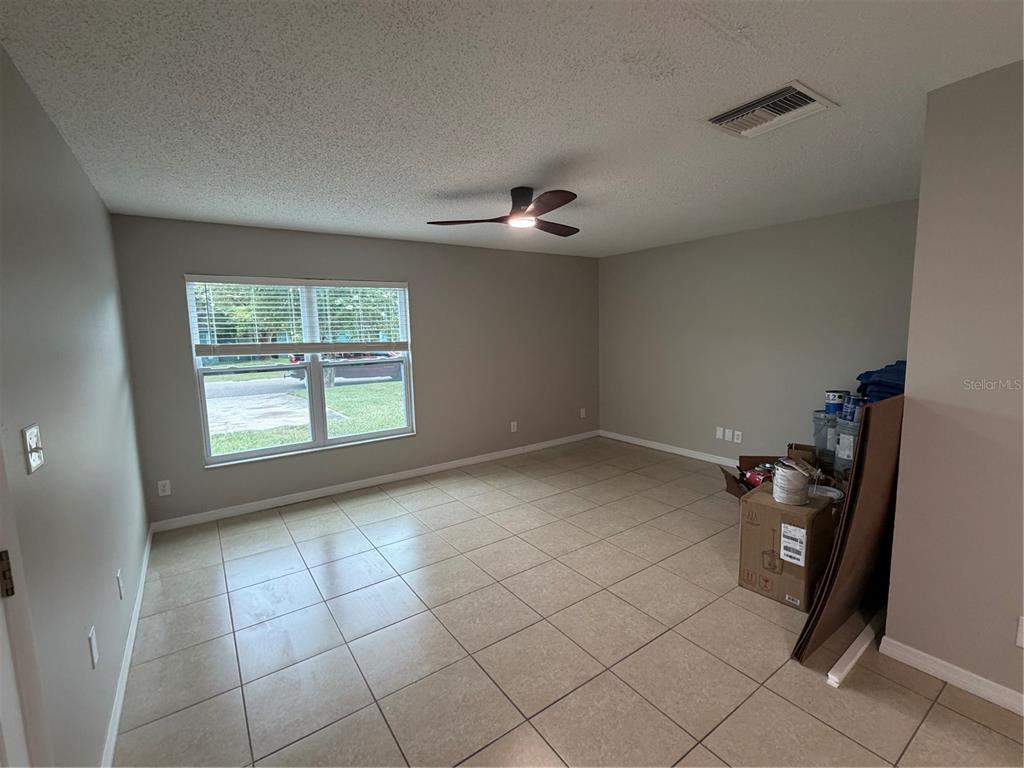 An empty room with beige tile flooring, a ceiling fan, and a large window — 11510 VALENCIA DR UNIT 2, SEFFNER, FL