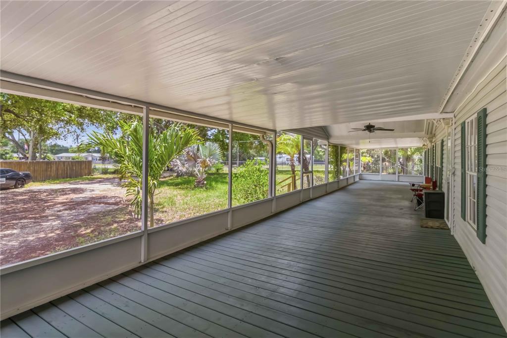 A long, covered screened-in porch features painted wooden decking and a ceiling fan — 12104 WOODSIDE DRIVE, RIVERVIEW, FL