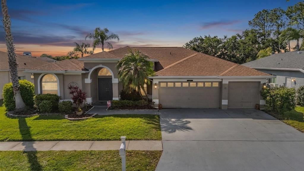 An aerial view shows a suburban house with a brown roof, driveway, and palm trees — 15922 MUIRFIELD DRIVE, ODESSA, FL