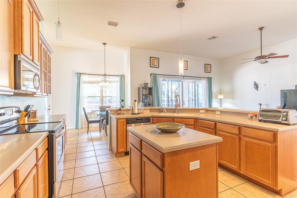 A kitchen with wood cabinets, a central island, and tile flooring opens to a living area — 2539 CENTENNIAL FALCON DRIVE, VALRICO, FL