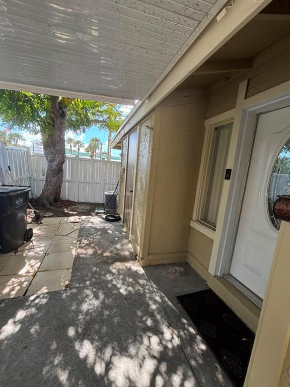 A concrete walkway leads to a front door under a covered patio next to a tree — 7310 BAJA COURT, TAMPA, FL
