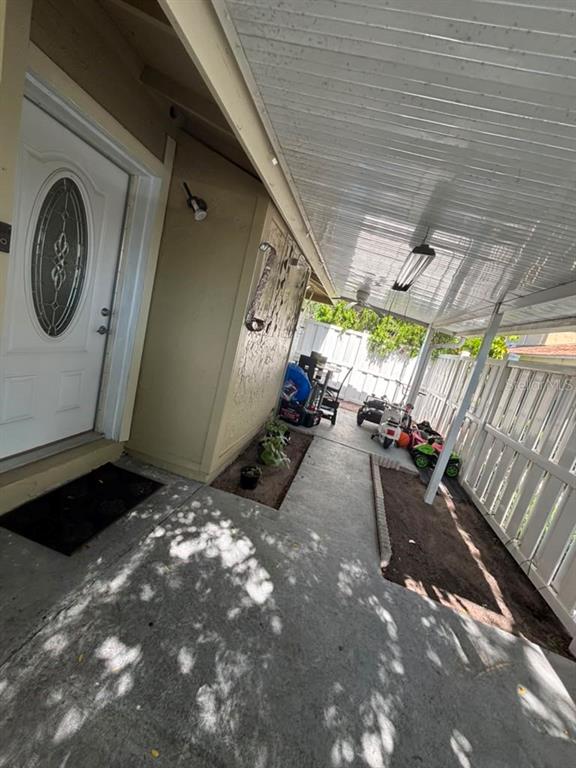 A concrete patio area features a covered walkway, a white front door, and small garden beds — 7310 BAJA COURT, TAMPA, FL