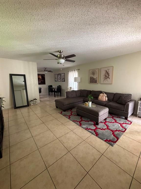 A living room features a gray sectional sofa, a patterned rug, and tile flooring — 7310 BAJA COURT, TAMPA, FL