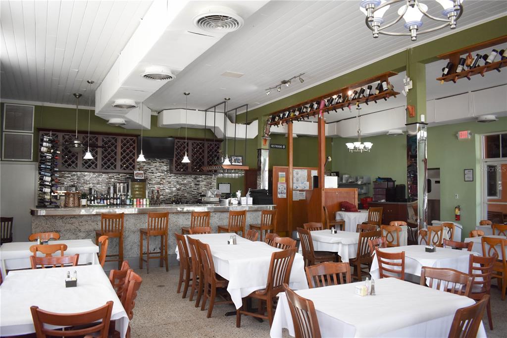A restaurant dining room features white-clothed tables, wooden chairs, a bar, and green walls — 1623 E 5TH AVENUE, TAMPA, FL