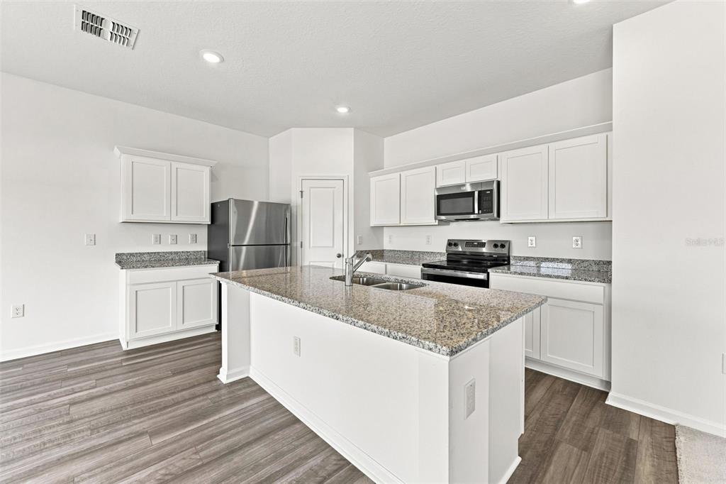 A kitchen with white cabinets, granite countertops, stainless steel appliances, and wood-look flooring — 8373 MARGO ANN STREET, BROOKSVILLE, FL