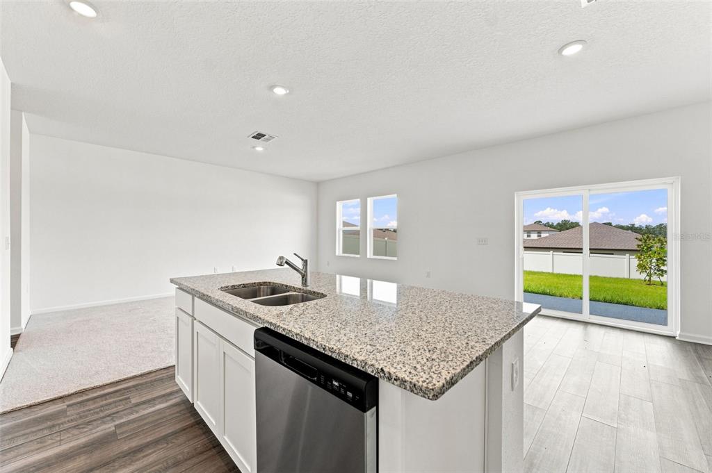 A kitchen island with a granite countertop and stainless steel dishwasher faces a sliding door — 8373 MARGO ANN STREET, BROOKSVILLE, FL