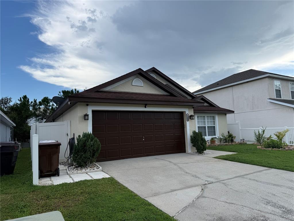 A single-story house features a brown two-car garage, a beige exterior, and a white fence — 4466 GREAT HARBOR LANE, KISSIMMEE, FL