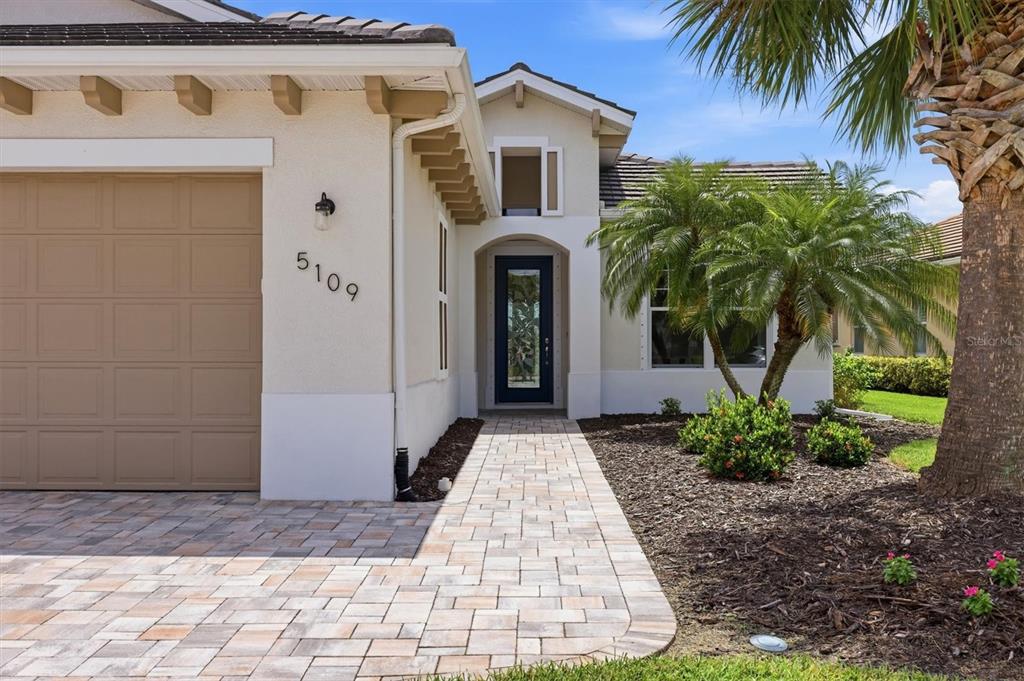 A single-story house exterior with a paved walkway, tan garage door, and palm tree — 5109 TIDEWATER PRESERVE BLVD, BRADENTON, FL