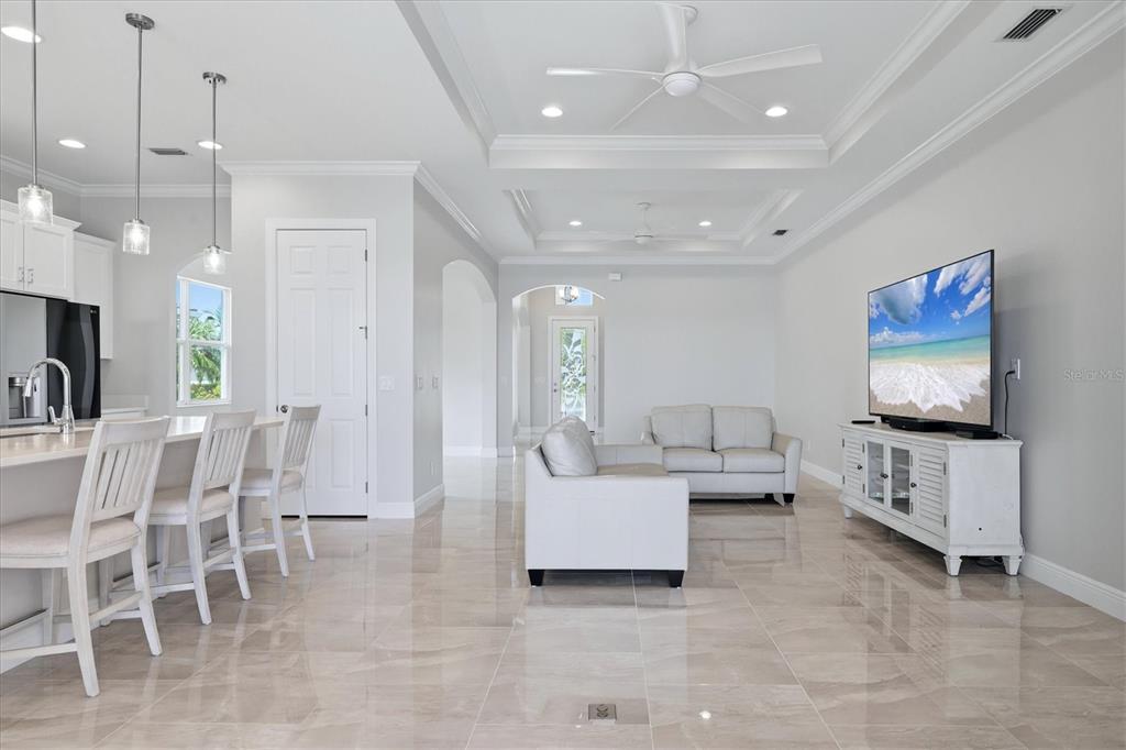 An open-concept living room and kitchen featuring white cabinetry, tile flooring, and a tray ceiling — 5109 TIDEWATER PRESERVE BLVD, BRADENTON, FL