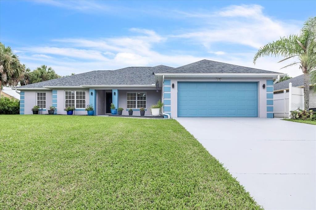 A single-story house with a blue garage door, gray exterior walls, and a manicured lawn — 1240 NORA LANE, NORTH PORT, FL