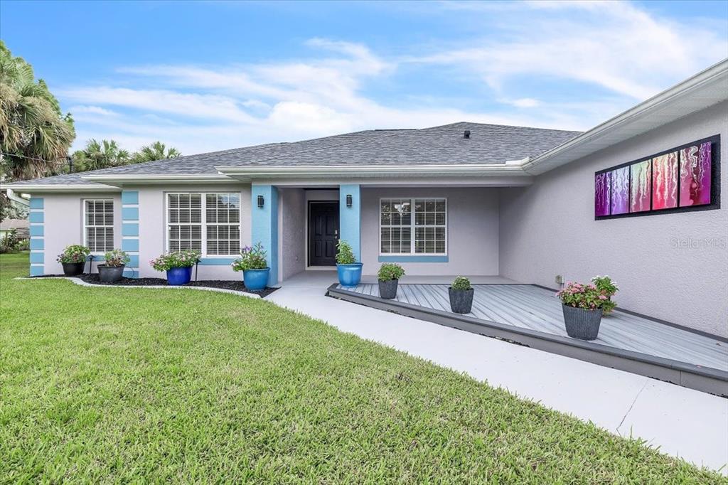 A single-story house exterior features a gray facade, blue accents, and a front wooden deck — 1240 NORA LANE, NORTH PORT, FL