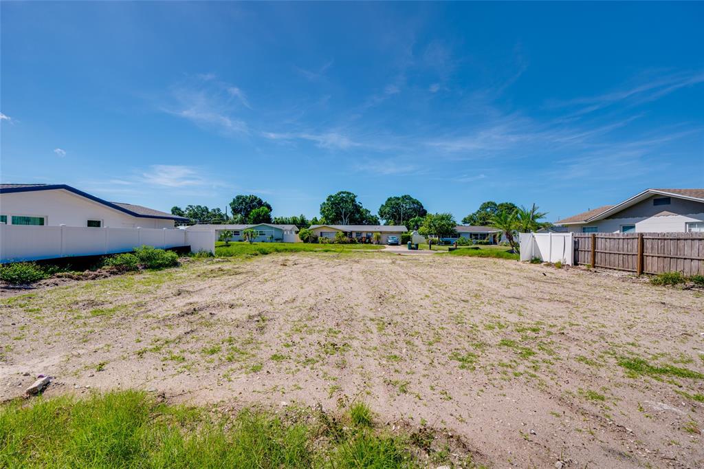 A vacant, sandy residential lot is enclosed by white and wooden fences under a blue sky — 13945 TRINIDAD DRIVE, SEMINOLE, FL