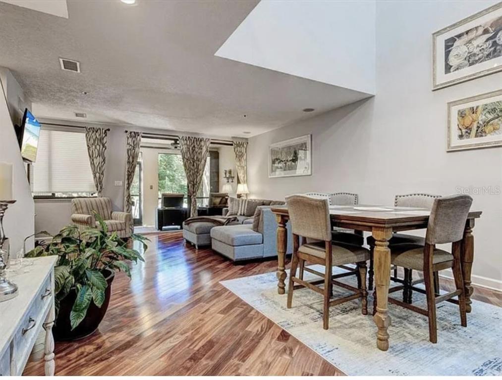 A dining area and living room with hardwood floors, vaulted ceilings, and neutral decor — 1926 HARBOURSIDE DRIVE UNIT 1302, LONGBOAT KEY, FL