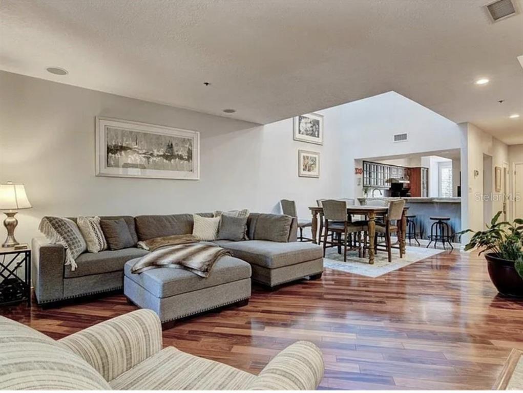 A living room with hardwood floors, a gray sectional sofa, and an adjacent dining area — 1926 HARBOURSIDE DRIVE UNIT 1302, LONGBOAT KEY, FL