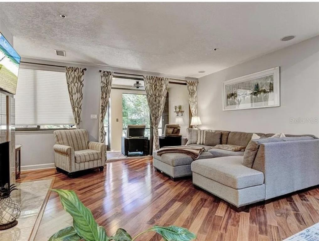 A living room with hardwood floors, a sectional sofa, an armchair, and a sliding glass door — 1926 HARBOURSIDE DRIVE UNIT 1302, LONGBOAT KEY, FL