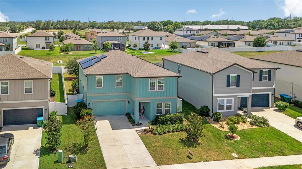 An aerial view shows a teal two-story house with solar panels next to neighboring homes — 1195 PEARL TREE ROAD, DELTONA, FL