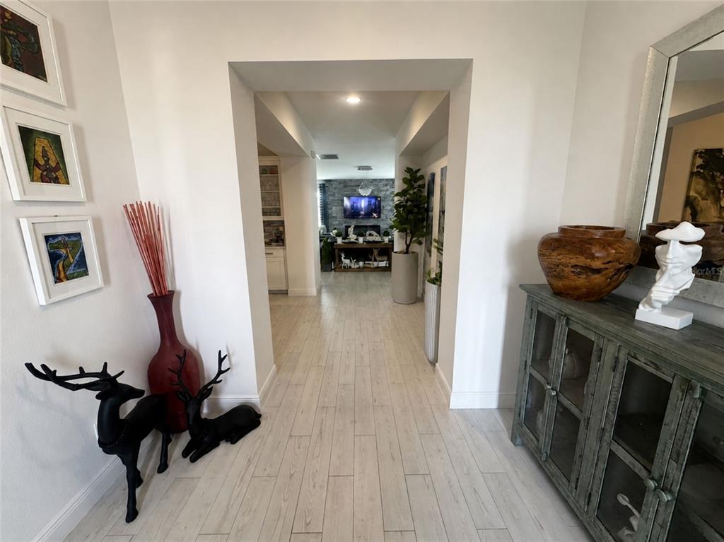 A hallway with light wood-look tile flooring leads toward a living area with a fireplace — 4938 CHASE COURT, ST CLOUD, FL