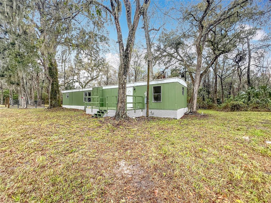A green mobile home sits on a grassy lot surrounded by large, moss-covered trees — 13026 SW WILLISTON ROAD, MICANOPY, FL