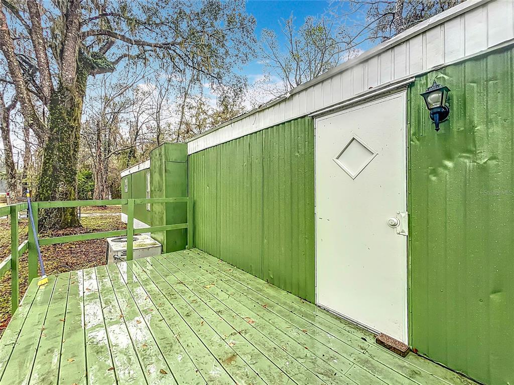 A green metal-sided mobile home features a wooden deck and a white door with a window — 13026 SW WILLISTON ROAD, MICANOPY, FL