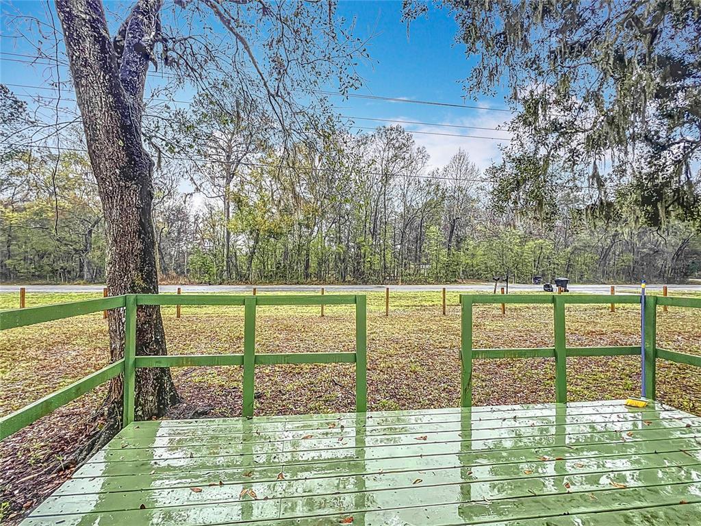 A green wooden deck with a railing overlooks a grassy yard and a wooded area — 13026 SW WILLISTON ROAD, MICANOPY, FL