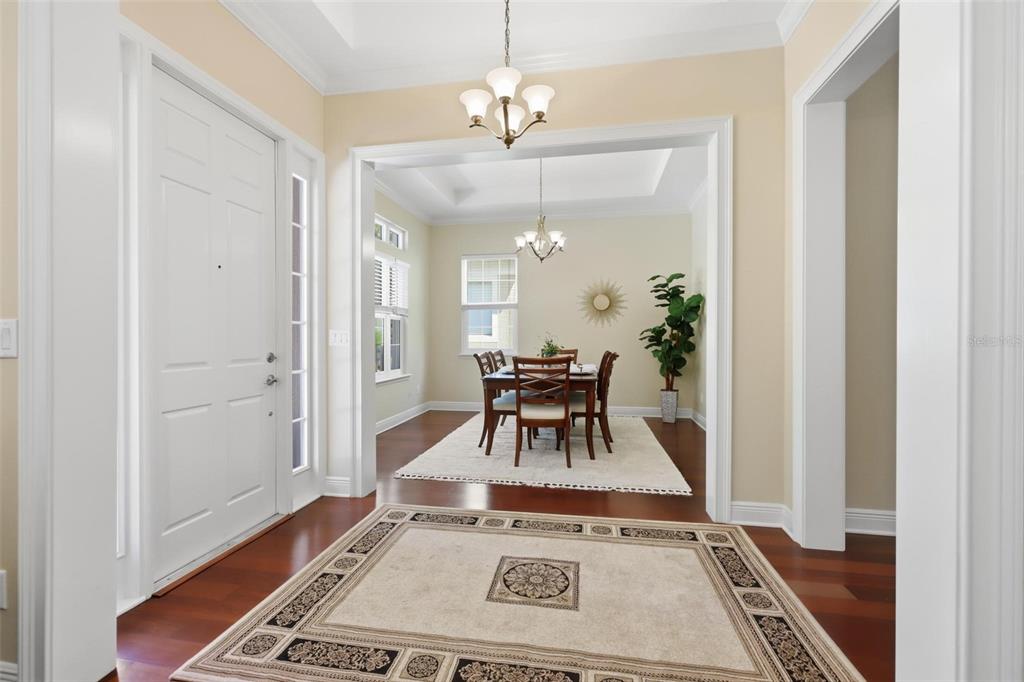 A foyer with hardwood floors and a rug leads into a dining room with chandeliers — 300 BELLINGRATH TERRACE, DELAND, FL